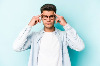 Kafkasyalı genç adam mavi arka planda izole edilmiş bir göreve odaklanmış, parmaklarını işaret ediyor..