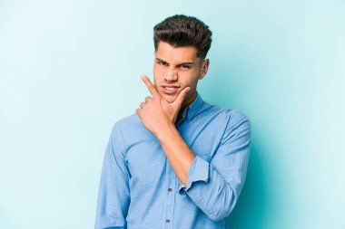 Kafkasyalı genç bir adam mavi arka planda izole edilmiş. Bir strateji planlıyor, bir iş yolu düşünüyor..