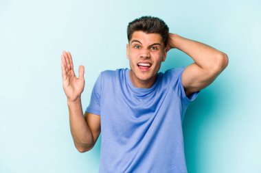 Mavi arka planda izole edilmiş genç beyaz adam öfkeyle bağırıyor..