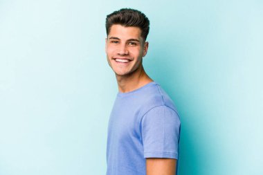 Kafkasyalı genç, mavi arka planda izole edilmiş. Kendine güvenen, kalçaları tutan biri..