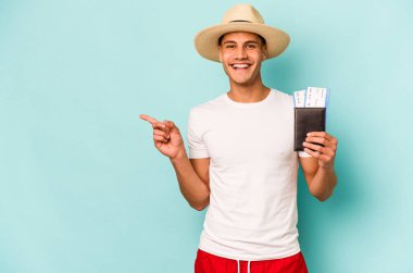 Pasaportu elinde tutan Kafkasyalı genç adam mavi arka planda izole edilmiş gülümsüyor ve boş alanda bir şey gösteriyor..