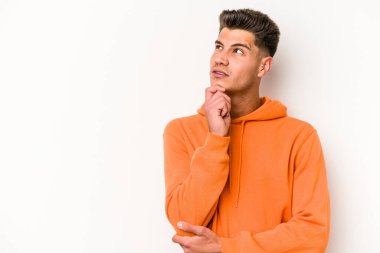 Beyaz arka planda izole edilmiş genç beyaz bir adam şüpheli ve şüpheci bir ifadeyle yana bakıyor..