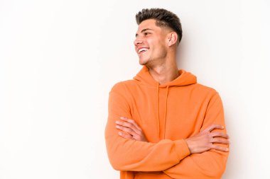 Beyaz arka planda izole edilmiş genç beyaz adam kollarını kavuşturarak gülümsüyor..