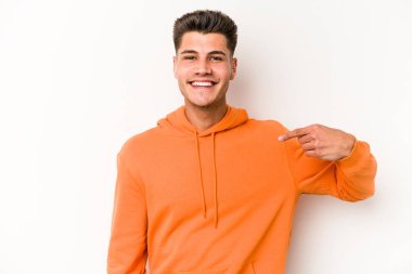 Beyaz arka planda yaşayan beyaz tenli genç bir adam gömlek fotokopi alanını gösteriyor, gururlu ve kendinden emin.