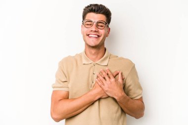 Beyaz arka planda soyutlanmış beyaz tenli genç bir adam gülüyor, elini yüreğine koyuyor, mutluluk kavramını koruyor..