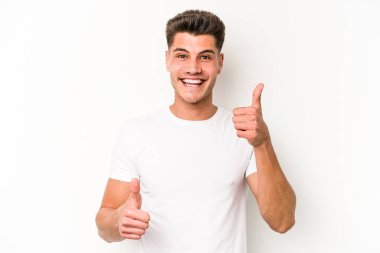 Beyaz arka planda izole edilmiş genç beyaz bir adam iki parmağını da kaldırıyor, gülümsüyor ve kendinden emin..