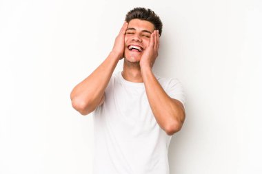 Beyaz arka planda izole olmuş genç beyaz bir adam ellerini başının üstünde tutarak neşeyle gülüyor. Mutluluk kavramı.