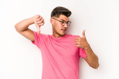 Beyaz arka planda izole edilmiş genç beyaz bir adam baş parmaklarını aşağı ve yukarı kaldırıyor, zor seçim konsepti