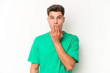Beyaz arka planda izole edilmiş genç beyaz adam şok olmuş, ağzı ellerle kaplanmış, yeni bir şey keşfetmeye hevesli..