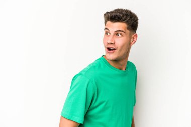 Beyaz arka planda izole edilmiş genç beyaz adam gülümseyen, neşeli ve keyifli bir tarafa bakıyor..