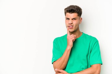 Beyaz arka planda izole edilmiş genç beyaz bir adam şüpheli ve şüpheci bir ifadeyle yana bakıyor..