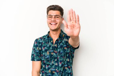 Beyaz arka planda izole edilmiş genç beyaz bir adam gülümseyerek beş numarayı parmaklarıyla gösteriyor..