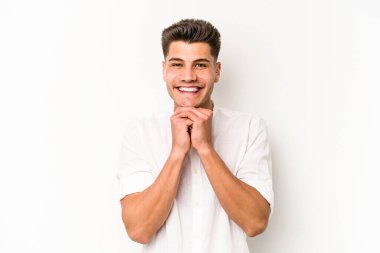 Beyaz arka planda izole genç beyaz adam ellerini çenesinin altında tutuyor, mutlu bir şekilde yana bakıyor..