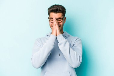 Mavi arka planda izole edilmiş genç beyaz bir adam el ele tutuşup, ağzının kenarında dua ediyor, kendinden emin..