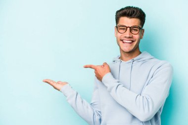 Kafkasyalı genç adam mavi arka planda izole edilmiş. Elinde palmiye ağacının bir kopyası olduğu için heyecanlı..