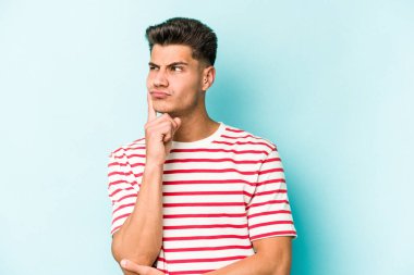 Kafkasyalı genç bir adam mavi arka planda izole edilmiş. Bir strateji planlıyor, bir iş yolu düşünüyor..