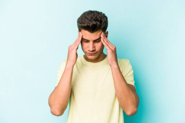 Genç beyaz adam mavi arka planda izole edilmiş tapınaklara dokunuyor ve başı ağrıyor..