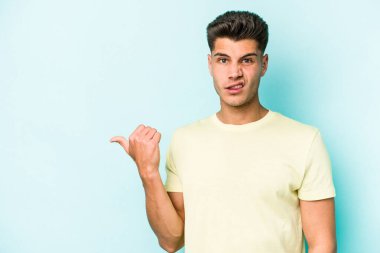 Mavi arka planda izole edilmiş genç beyaz adam işaret parmağıyla fotokopi alanını işaret ederek şok oldu..