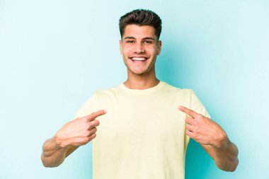 Kafkasyalı genç adam mavi arka planda izole edildi. Parmakları aşağıda, olumlu bir his var..