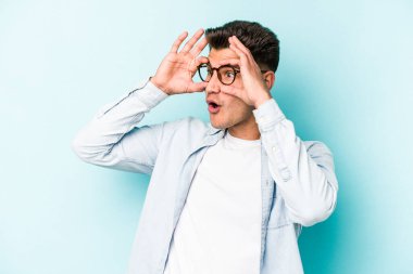 Mavi arka planda izole edilmiş genç beyaz adam bir başarı fırsatı bulmak için gözlerini açık tutuyor..