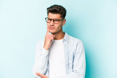 Mavi arka planda izole edilmiş genç beyaz adam alaycı bir ifadeyle kameraya bakarken mutsuz oluyor..