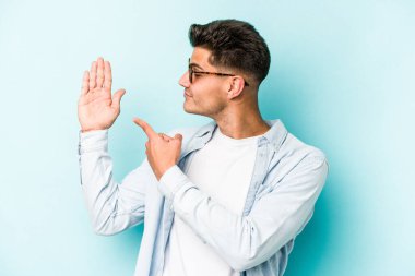 Mavi arka planda izole edilmiş genç beyaz adam gülümseyerek beş numarayı parmaklarıyla gösteriyor..