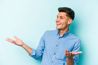 Kafkasyalı genç adam mavi arka planda izole edilmiş neşeli bir şekilde gülüyor. Mutluluk kavramı.