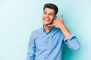 Mavi arka planda izole edilmiş genç beyaz adam parmaklarıyla bir cep telefonu hareketi gösteriyor..
