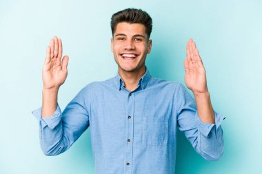 Kafkasyalı genç adam mavi arka planda izole edilmiş. Elinde işaret parmaklarıyla küçük bir şey tutuyor, gülümsüyor ve kendinden emin..