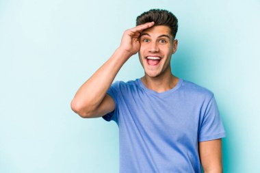 Mavi arka planda izole edilmiş genç beyaz adam yüksek sesle bağırıyor, gözleri açık ve elleri gergin tutuyor..