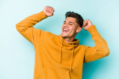 Mavi arka planda izole genç beyaz adam özel bir günü kutluyor, atlıyor ve enerjiyle kollarını kaldırıyor..