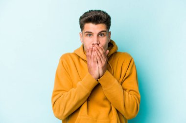 Kafkasyalı genç adam mavi arka planda izole edilmiş ağzı kapalı ve elleri endişeli görünüyor..