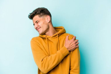 Mavi arka planda izole edilmiş, omuz ağrısı olan genç beyaz bir adam..