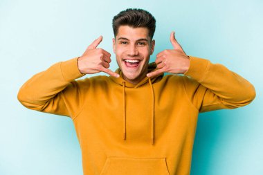 Mavi arka planda izole edilmiş genç beyaz adam parmaklarıyla bir cep telefonu hareketi gösteriyor..