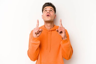 Beyaz arka planda izole edilmiş genç beyaz adam ağzı açık bir şekilde üst tarafı işaret ediyor..