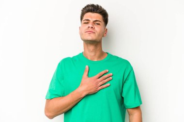 Beyaz arka planda izole edilmiş genç beyaz adam yemin ediyor, elini göğsüne koyuyor..