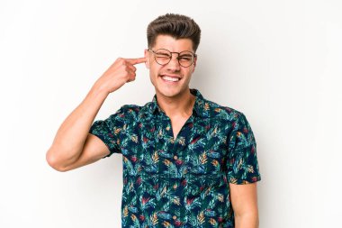 Beyaz arka planda izole edilmiş genç beyaz bir adam kulaklarını elleriyle kapatıyor..