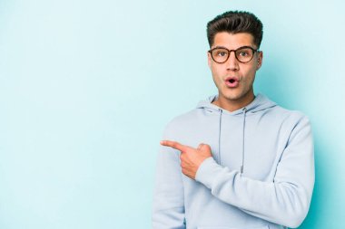 Mavi arka planda izole edilmiş genç beyaz adam yan tarafı işaret ediyor.
