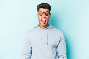 Kafkasyalı genç adam mavi arka planda izole edilmiş komik ve dost canlısı bir dil uzatıyor..