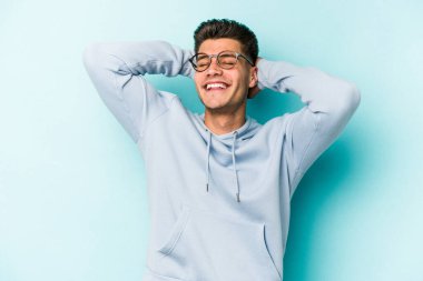 Mavi arka planda izole edilmiş genç beyaz adam kollarını uzatıyor, rahat bir konumda..