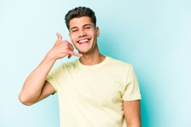 Mavi arka planda izole edilmiş genç beyaz adam parmaklarıyla bir cep telefonu hareketi gösteriyor..