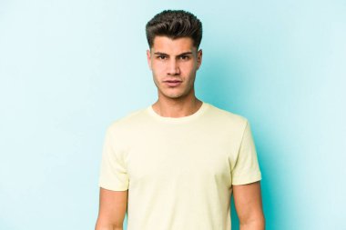 Kafkasyalı genç adam mavi arka planda izole edilmiş üzgün, ciddi yüzlü, mutsuz ve hoşnutsuz..