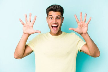 Mavi arka planda izole edilmiş genç beyaz adam hoş bir sürpriz alıyor, heyecanlı ve el kaldırıyor..