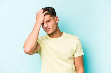 Kafkasyalı genç adam mavi arka planda izole edilmiş bir şekilde bir şeyi unutuyor. Alnına avuç içi ve gözlerini kapayarak vuruyor..