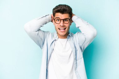 Mavi arka planda izole edilmiş genç beyaz adam öfkeyle bağırıyor..