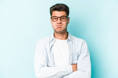 Mavi arka planda izole edilmiş genç beyaz adamın yanakları şişer, yorgun bir ifadesi vardır. Yüz ifadesi kavramı.