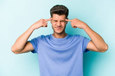 Kafkasyalı genç adam mavi arka planda izole edilmiş bir göreve odaklanmış, parmaklarını işaret ediyor..