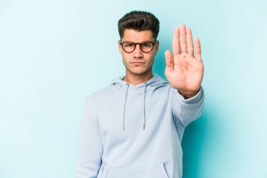 Mavi arka planda izole edilmiş genç beyaz adam elini uzatmış, dur işareti göstererek seni engelliyor..
