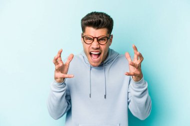 Mavi arka planda izole edilmiş genç beyaz adam öfkeyle bağırıyor..