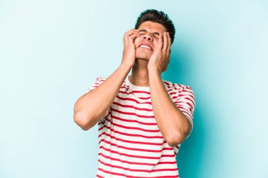 Kafkasyalı genç adam mavi arka planda izole edilmiş, ağlıyor, bir şeyden memnun değil, acı ve kafa karışıklığı konsepti..